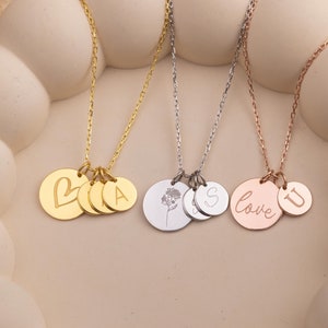May include: Three gold necklaces with different charms. The first necklace has a heart charm, a small circle charm, and a charm with the letter "A". The second necklace has a charm with a small flower, a charm with the letter "S", and a charm with a heart. The third necklace has a charm with the word "love" and a charm with the letter "U".