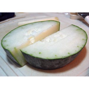 May include: Two halves of a light green winter melon, cut in half and sliced, on a white cutting board.