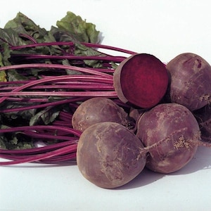 May include: A bunch of red beets with green leafy tops. The beets are arranged in a pile, with one beet cut in half to show the red flesh.
