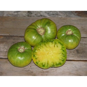 May include: Four green tomatoes, one sliced in half to reveal a yellow interior with green veins. The tomatoes are on a wooden surface.