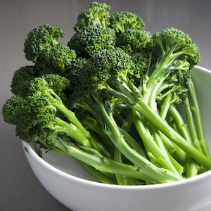 May include: A white bowl filled with fresh, green broccoli florets. The broccoli is arranged in a cluster, with the stems facing outwards.