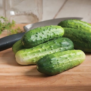 May include: A group of five green cucumbers on a wooden cutting board. The cucumbers are fresh and have a bumpy texture.