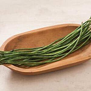 May include: A wooden bowl filled with a bunch of long, green string beans.