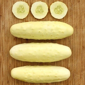 May include: Three whole white cucumbers and three cucumber slices on a wooden cutting board.