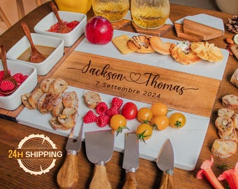 May include: A white marble and wood serving board with a personalized inscription: "Jackson & Thomas 7 Settembre 2024". The board is surrounded by various snacks, including bread, fruit, and cookies. Four cheese knives are also included.