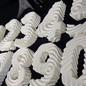 May include: A selection of white, abstract sculptures with a layered, wave-like design. The forms are arranged on a dark surface, creating a contrast that highlights their intricate details. The sculptures appear to be decorative or artistic elements.