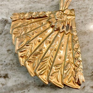 May include: A gold-toned metal decorative tray with a fan-shaped design. The tray has a raised floral design and a scalloped edge.