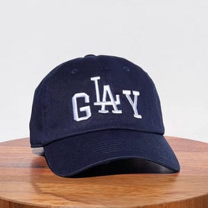 May include: A navy blue baseball cap with a white embroidered "G.L.A.Y." logo.