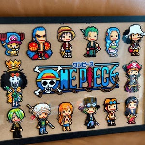 May include: A framed pixel art piece showcasing characters from the anime "One Piece." The artwork presents a grid of characters, alongside the series' logo. The characters are depicted in a colourful, blocky style, reminiscent of retro video games.