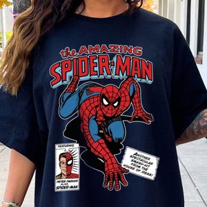 Może przedstawiać: Granatowa koszulka z komiksową ilustracją Spider-Mana. Projekt zawiera tekst "the AMAZING SPIDER-MAN" w kolorze czerwonym i niebieskim oraz dodatkowe dymki. Superbohater jest przedstawiony w swoim klasycznym czerwono-niebieskim kostiumie.