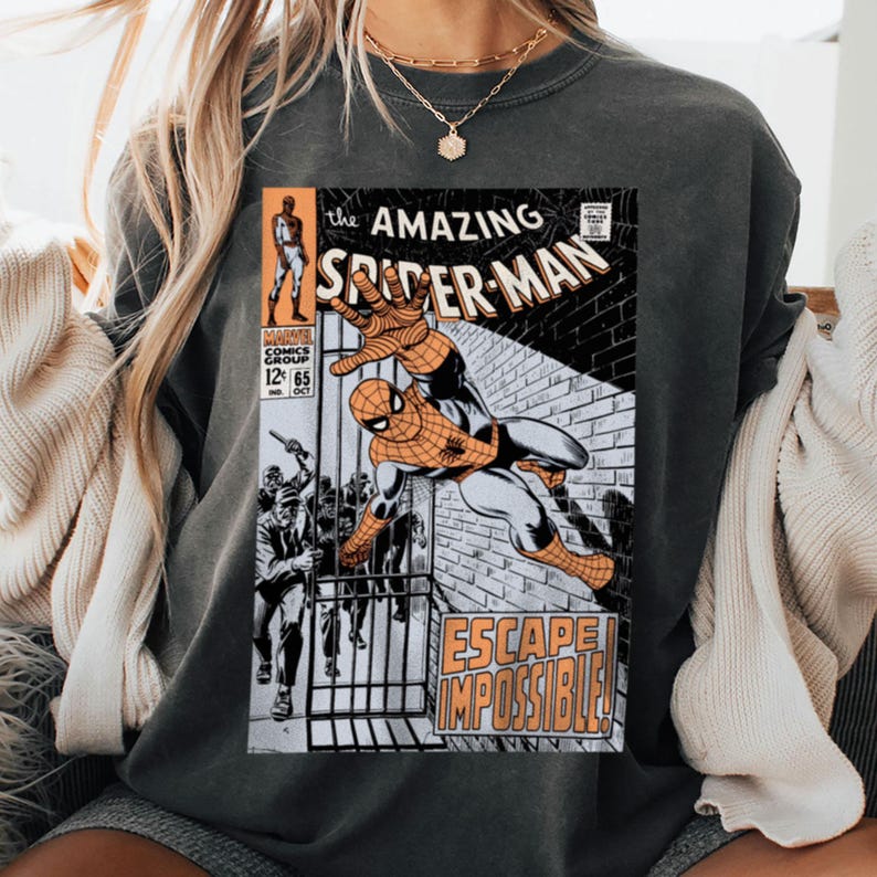 May include: Dark gray sweatshirt featuring a vintage comic book cover of The Amazing Spider-Man. The comic art shows Spider-Man in action with the words "ESCAPE IMPOSSIBLE!" and "The Amazing Spider-Man" printed on the front.