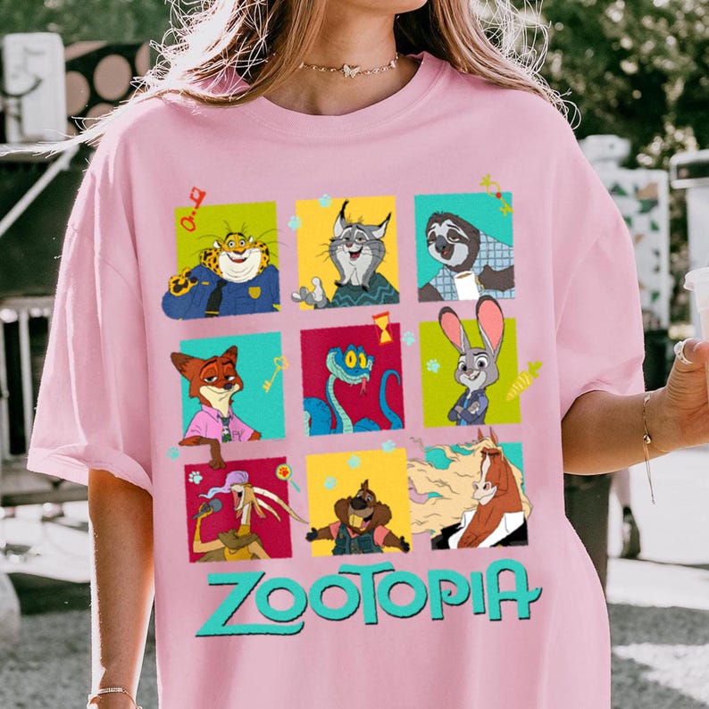 Puede incluir: Camiseta rosa claro con una cuadr&iacute;cula de personajes de dibujos animados de la pel&iacute;cula Zootopia. Los personajes est&aacute;n en cuadrados coloridos, con la palabra "Zootopia" en turquesa debajo.