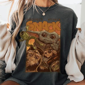 May include: Dark gray sweatshirt featuring a graphic of Grogu, other Star Wars characters, and the word "SNACK" in orange letters. The sweatshirt has a vintage, faded look.
