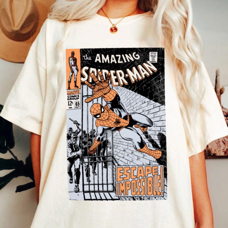 May include: Cream-colored t-shirt featuring a vintage comic book cover of Spider-Man. The comic art shows Spider-Man in action with the words "The Amazing Spider-Man" and "Escape Impossible!" printed on the front.