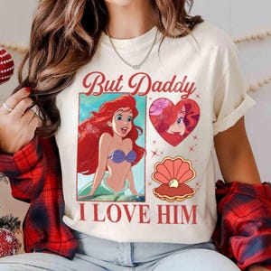 May include: A white t-shirt featuring a graphic print of Ariel from The Little Mermaid. The graphic includes the text "But Daddy I Love Him".