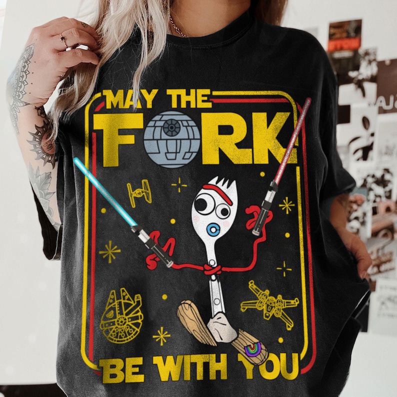 May include: Black t-shirt with a humorous graphic featuring a fork character with lightsabers and a pacifier. The design includes the text "MAY THE FORK BE WITH YOU" in a yellow and red frame, with Star Wars-themed elements.