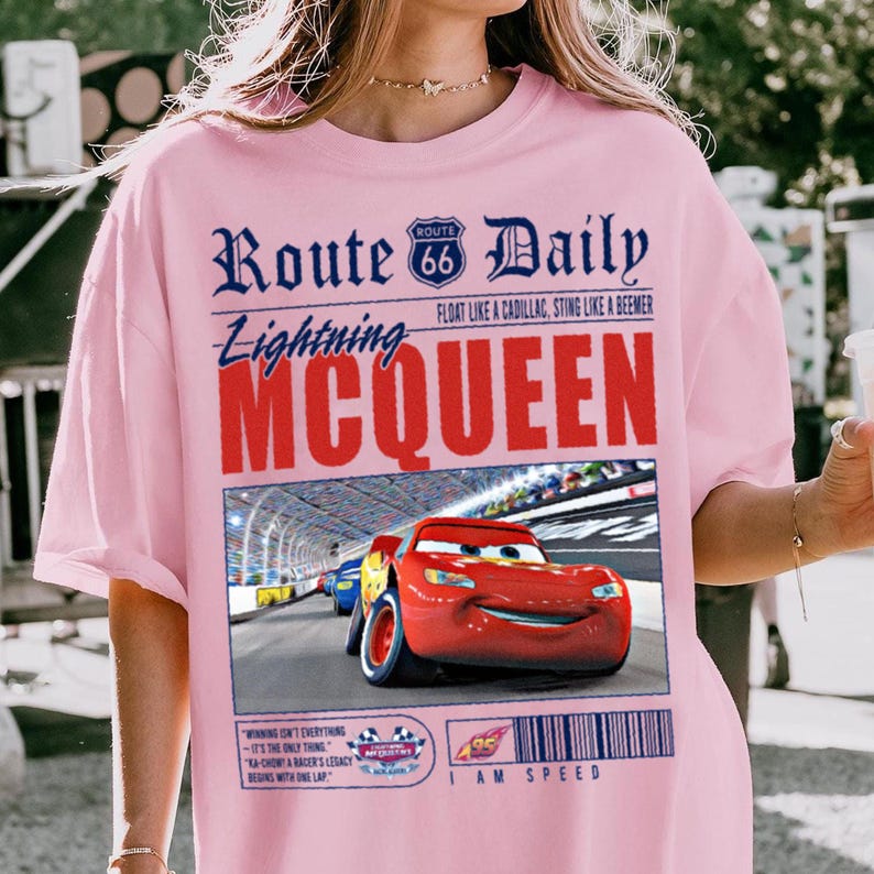 Op de afbeelding: Roze T-shirt met een afbeelding van Lightning McQueen uit de film Cars. De afbeelding bevat de tekst "Route 66 Daily" en "I am Speed".