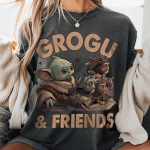 K&ouml;nnte beinhalten: Dunkelgraues Sweatshirt mit dem Schriftzug "GROGU & FRIENDS" in Beige. Die Grafik zeigt Grogu und andere Charaktere aus Star Wars. Gedruckt auf einem weichen, bequemen Stoff.