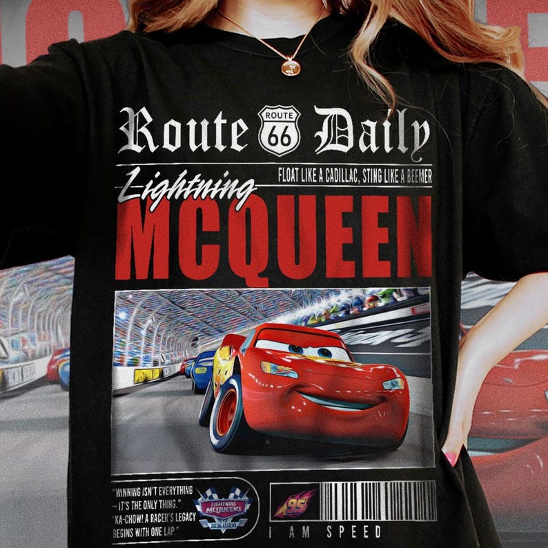 Op de afbeelding: Zwart T-shirt met een afbeelding van Lightning McQueen uit de film Cars. De afbeelding heeft een krantenstijl ontwerp met de tekst "Route 66 Daily" en "Lightning McQueen". De afbeelding bevat ook een citaat uit de film: "Winnen is niet alles - het is het enige." en "Ka-chow! De erfenis van een coureur begint met een ronde."