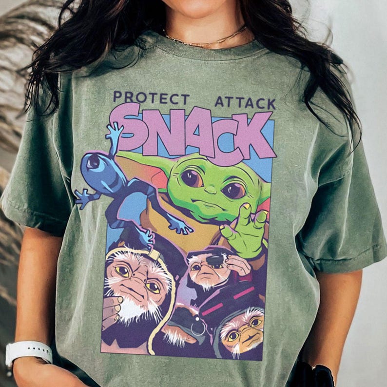 K&ouml;nnte beinhalten: Gr&uuml;nes T-Shirt mit einem farbenfrohen Aufdruck mit dem Text "PROTECT ATTACK SNACK". Die Grafik zeigt eine gr&uuml;ne Alien-Figur, einen blauen Alien und andere Zeichentrickfiguren. Das T-Shirt hat einen l&auml;ssigen Stil.