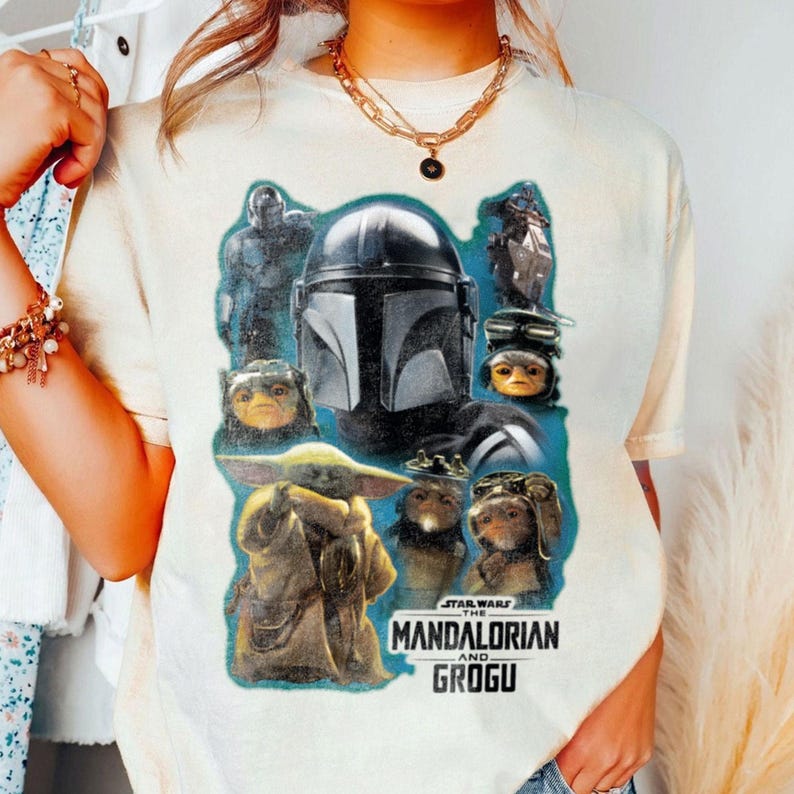 May include: A cream-coloured t-shirt displaying a graphic from the Star Wars series, "The Mandalorian and Grogu." The design incorporates characters such as Grogu and the Mandalorian's helmet, set against a blue backdrop. The text "STAR WARS THE MANDALORIAN AND GROGU" is also present.