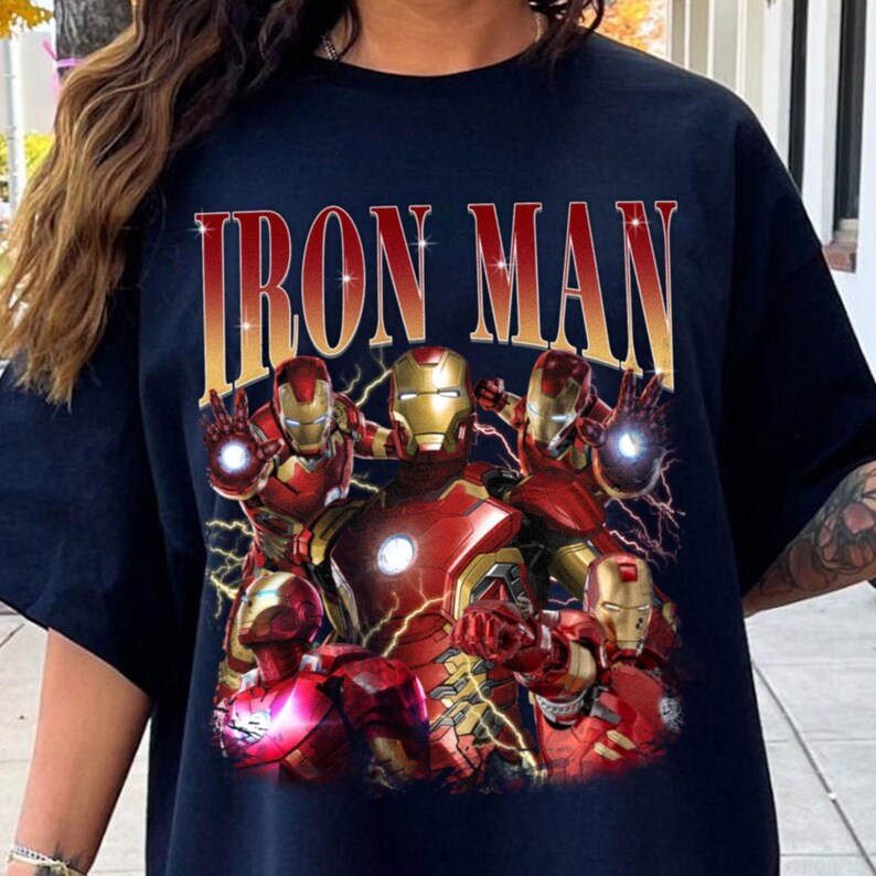 Puede incluir: Camiseta azul marino con un dise&ntilde;o de Iron Man en rojo y dorado. El dise&ntilde;o presenta m&uacute;ltiples figuras de Iron Man y el texto "IRON MAN" en dorado, con un efecto desgastado.