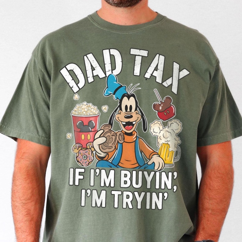 Op de afbeelding: Olijfgroen T-shirt met de tekst "DAD TAX" boven een cartoonafbeelding van Goofy, omringd door snacks en bier. De tekst "IF I'M BUYIN', I'M TRYIN'" staat onder de afbeelding.