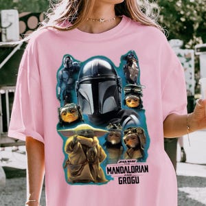 May include: Pale pink t-shirt with a graphic print of characters from The Mandalorian. The design includes The Mandalorian, Grogu, and other creatures, with the text "STAR WARS THE MANDALORIAN AND GROGU" in white.