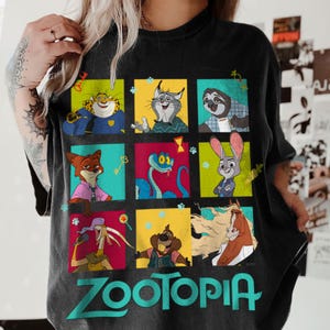Puede incluir: Camiseta negra con una cuadr&iacute;cula de personajes de Zootopia en cuadrados de colores. La palabra "Zootopia" est&aacute; impresa en turquesa en la parte inferior. La camiseta presenta personajes de la pel&iacute;cula animada.