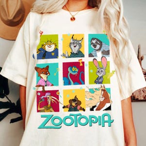 Puede incluir: Camiseta color crema con un gr&aacute;fico colorido de personajes de la pel&iacute;cula animada "Zootr&oacute;polis". El dise&ntilde;o incluye nueve paneles cuadrados con varios personajes de animales y la palabra "Zootopia" en letras turquesas en la parte inferior. La camiseta es de material suave.
