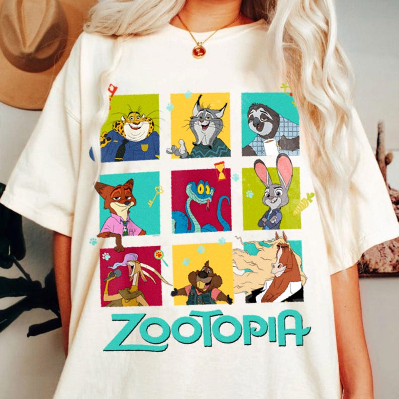 Puede incluir: Camiseta color crema con un gr&aacute;fico colorido de personajes de la pel&iacute;cula animada "Zootr&oacute;polis". El dise&ntilde;o incluye nueve paneles cuadrados con varios personajes de animales y la palabra "Zootopia" en letras turquesas en la parte inferior. La camiseta es de material suave.