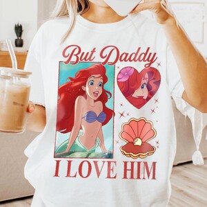 May include: White t-shirt featuring a red, white and blue graphic print of Ariel from The Little Mermaid. The graphic includes the text "But Daddy I Love Him".
