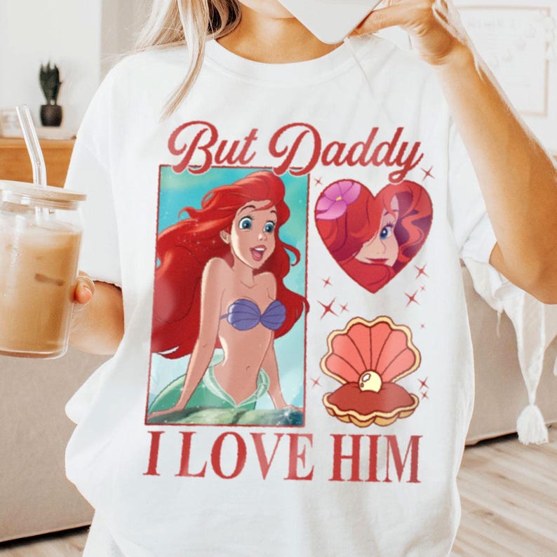 May include: White t-shirt featuring a red, white and blue graphic print of Ariel from The Little Mermaid. The graphic includes the text "But Daddy I Love Him".