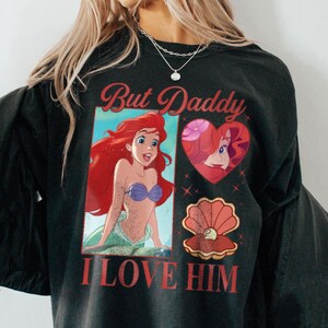 May include: Black long-sleeved shirt with a graphic print of Ariel from The Little Mermaid. The text "But Daddy I Love Him" is printed in red on the shirt.