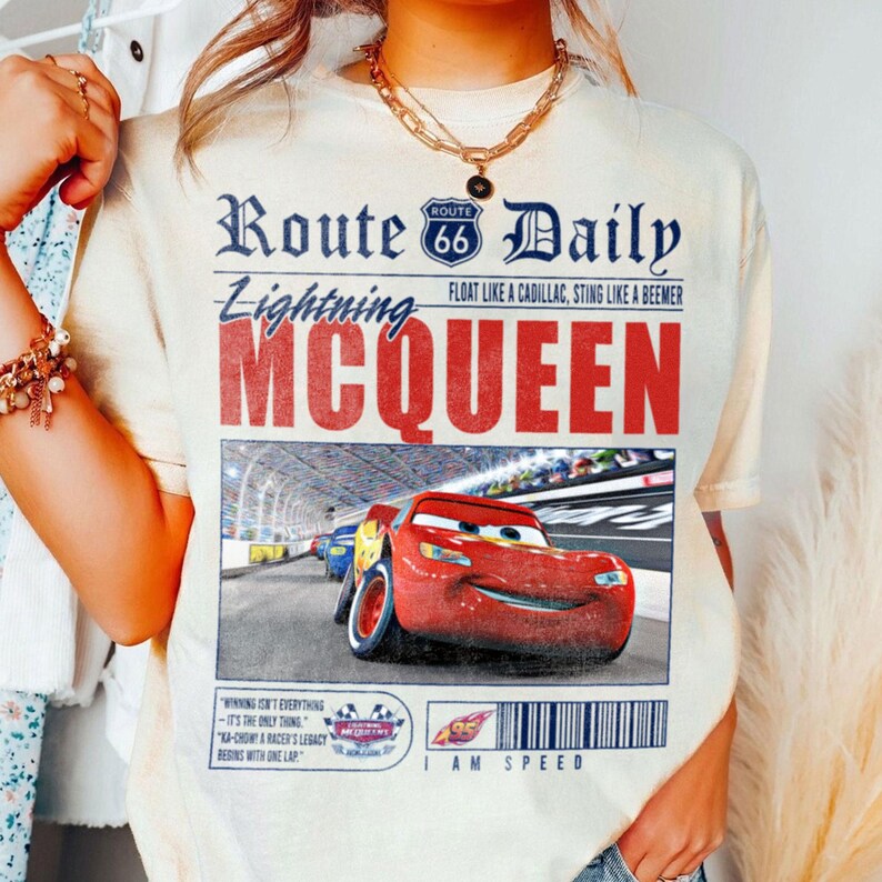 Op de afbeelding: Een wit T-shirt met een vintage krantenontwerp met een rode raceauto met de tekst "Route 66 Daily", "Lightning McQueen" en "I am Speed".