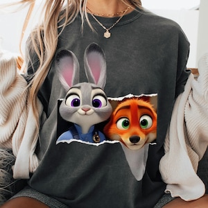 May include: Dark gray sweatshirt featuring a graphic of Judy Hopps and Nick Wilde from Zootopia. Judy is a gray bunny with purple eyes, and Nick is an orange fox with green eyes. The graphic appears to be torn out of the sweatshirt.