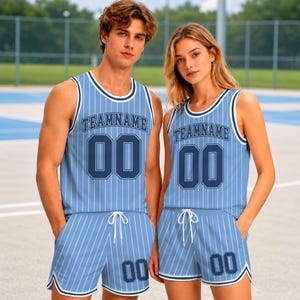 May include: A light blue basketball jersey and shorts set featuring thin white vertical pinstripes, dark blue trim, and the text TEAMNAME with the number 00 printed in dark blue on the chest and the shorts. The set has a drawstring waistband.