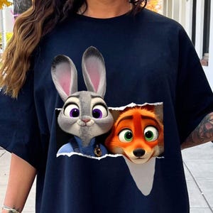 May include: Navy blue t-shirt featuring a graphic of Judy Hopps and Nick Wilde from Zootopia. Judy, a gray rabbit with purple eyes, is on the left, and Nick, an orange fox with green eyes, is on the right. The design appears to be torn out of the shirt.