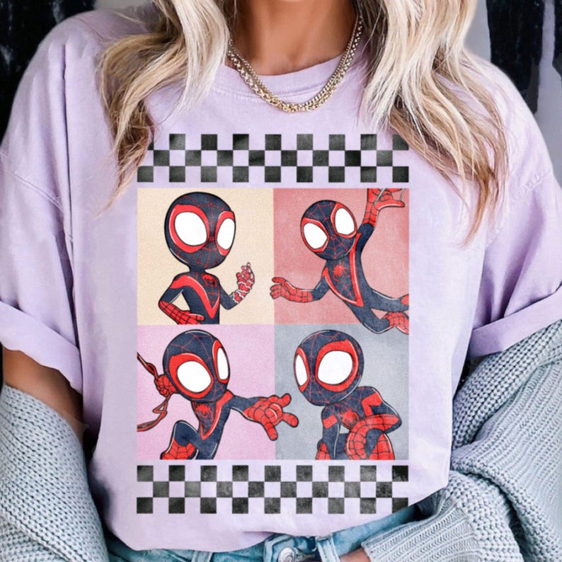 Puede incluir: Una camiseta de color lila claro con un gr&aacute;fico de cuatro paneles de un superh&eacute;roe de dibujos animados con un traje negro y rojo y una m&aacute;scara blanca. El gr&aacute;fico est&aacute; enmarcado con un patr&oacute;n de cuadros blanco y negro.