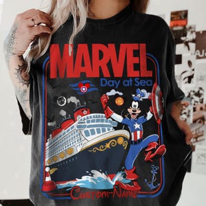 May include: Black t-shirt with a Marvel Day at Sea graphic. The design features a cruise ship, Mickey Mouse as Captain America, and the text "MARVEL" in red. The shirt has a vintage, distressed look.