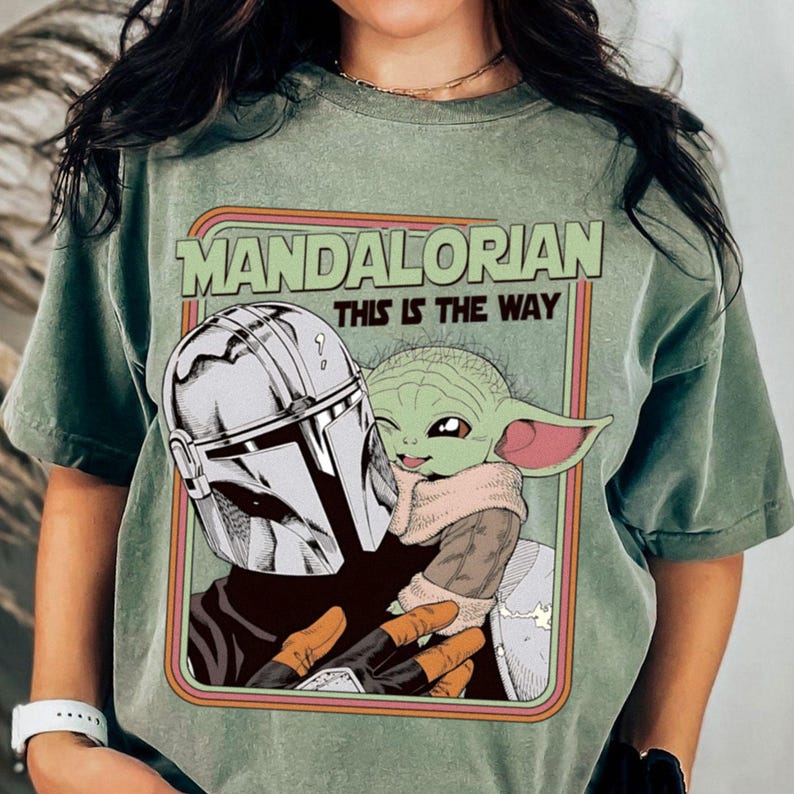 Puede incluir: Camiseta verde con un gr&aacute;fico de The Mandalorian y Grogu. El dise&ntilde;o incluye el texto "MANDALORIAN" encima de "THIS IS THE WAY" en un marco de estilo retro. La camiseta es de color verde liso.