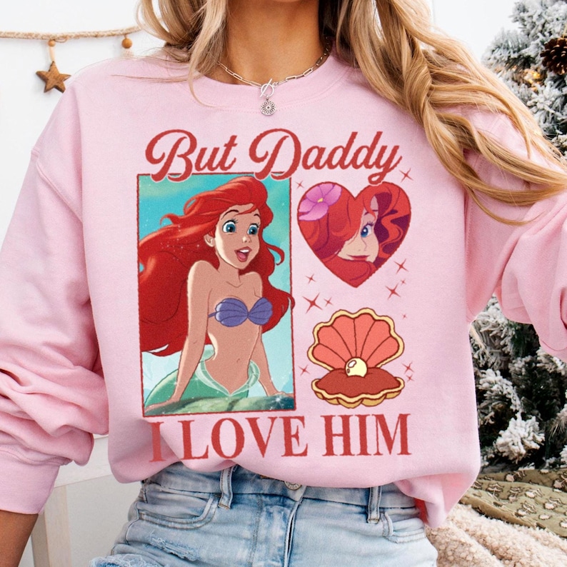 May include: Pink sweatshirt with a graphic print of Ariel from The Little Mermaid. The text "But Daddy I Love Him" is printed on the sweatshirt.