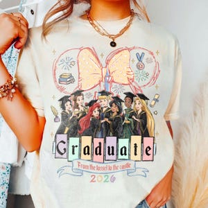 Puede incluir: Camiseta color crema con un gr&aacute;fico de princesas de Disney con atuendo de graduaci&oacute;n. El dise&ntilde;o incluye un gran lazo, s&iacute;mbolos de graduaci&oacute;n y el texto "Graduate From the tassel to the castle 2026".