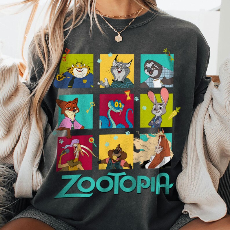Puede incluir: Sudadera gris oscuro con una cuadr&iacute;cula colorida de personajes de Zootopia. Cada cuadrado muestra un personaje diferente, con la palabra "Zootopia" impresa en turquesa debajo. Cuello redondo.