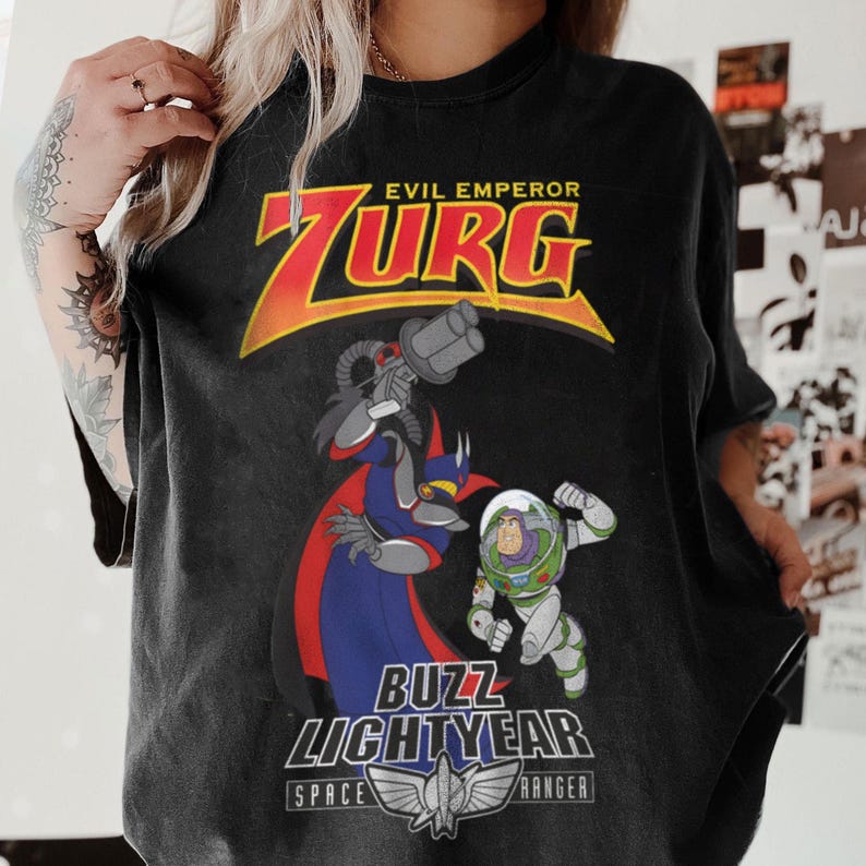 May include: Black t-shirt featuring a graphic of Evil Emperor Zurg and Buzz Lightyear from Toy Story. The design includes the text "EVIL EMPEROR ZURG" in yellow and red, and "BUZZ LIGHTYEAR SPACE RANGER" below the characters.
