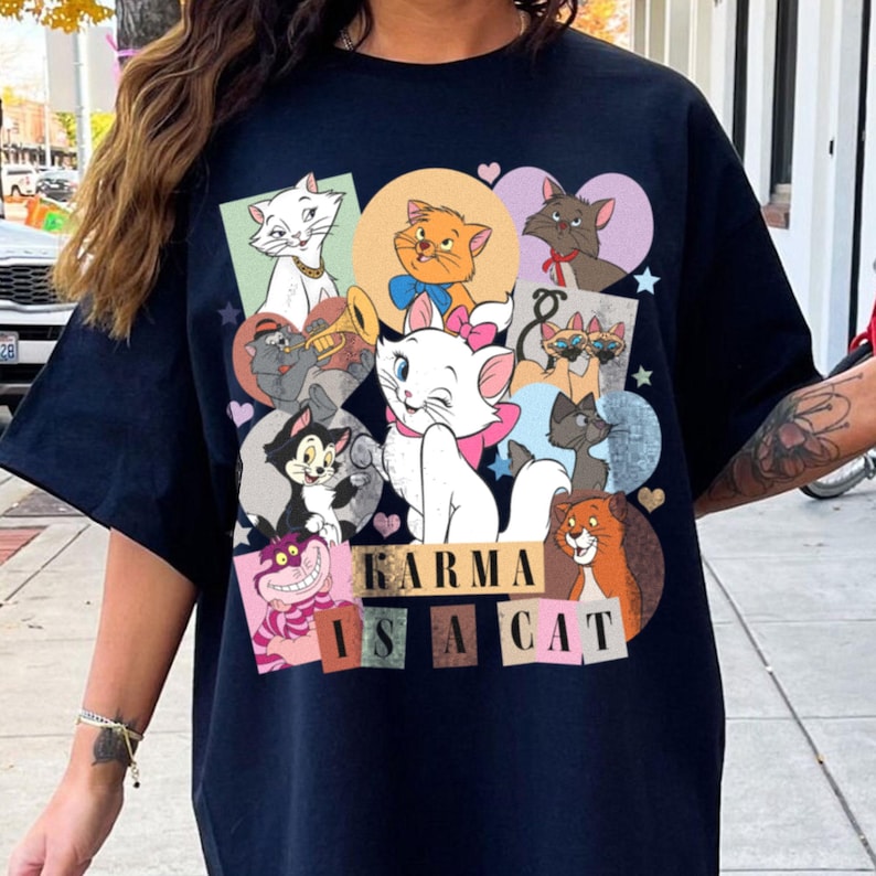 Puede incluir: Camiseta negra con un estampado gr&aacute;fico colorido de varios gatos de dibujos animados. El texto "KARMA IS A CAT" est&aacute; impreso en la parte inferior de la camiseta.