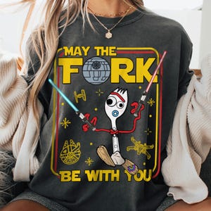 May include: Dark gray sweatshirt with a colorful graphic featuring a fork character with lightsabers, a Death Star, and the text "MAY THE FORK BE WITH YOU". The design is framed in yellow and red.