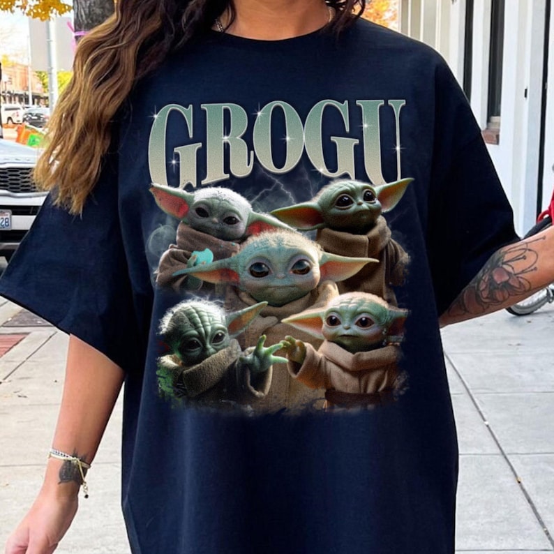 May include: Dark blue t-shirt with the word "GROGU" in light green. The graphic shows five Grogu characters, each with large ears and brown robes, set against a stormy background. A casual, comfortable top.