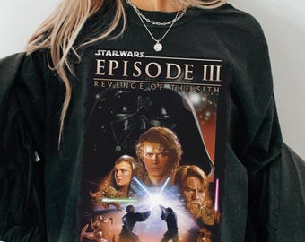 May include: Black crew neck t-shirt featuring the Star Wars Episode III: Revenge of the Sith movie poster. The graphic includes Darth Vader, Anakin Skywalker, Obi-Wan Kenobi, and other characters from the film. The Star Wars logo is at the top.