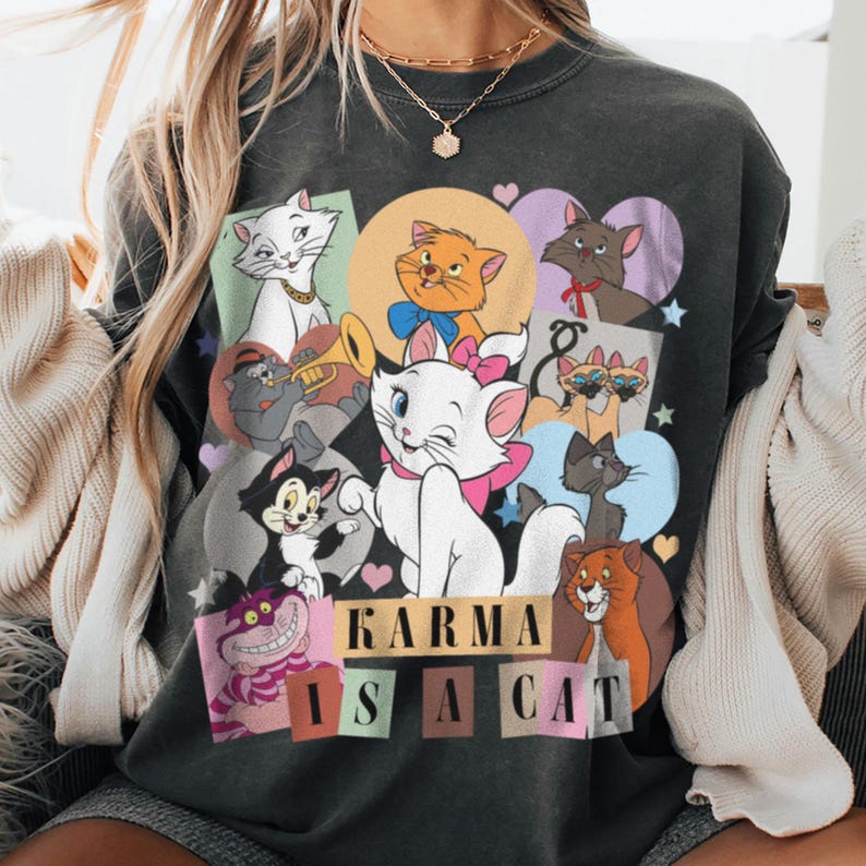 Puede incluir: Camiseta negra con un estampado gr&aacute;fico de varios gatos de dibujos animados. El texto "Karma is a cat" est&aacute; impreso en la parte inferior de la camiseta.